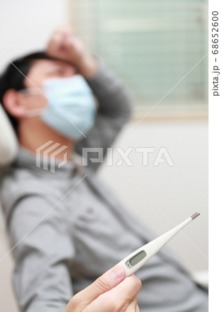 マスクをして体温を測る体調不良のカジュアル男性 68652600