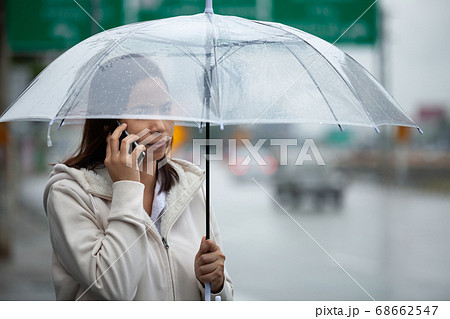 Asian woman talking on a cell phone and holding umbrella while standing on the city street Asian woman talking on a cell phone and holding umbrella while standing on the city street 68662547