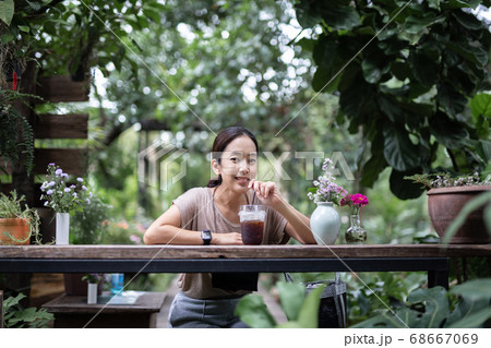 Woman resting outdoors sitting on wooden chair drinking iced coffee in nature garden. 68667069