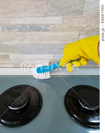 woman's hand in a rubber glove washes the gas stove with a brush. The concept of cleaning 68667460