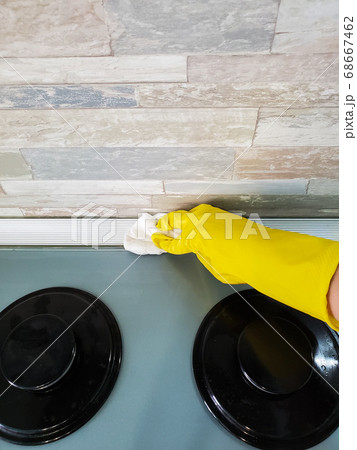 Hand in protective gloves cleans the gas stove with a rag 68667462