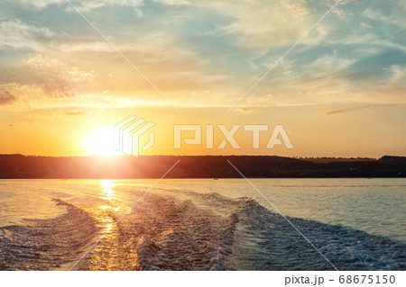 Scenic bright vibrant blue to red warm sunset evening time landscape with motorbaot swirl trace on water surface of lake or river. Horizon coast line on background 68675150