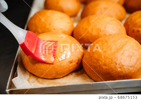 Smearing buns with egg yolk with kitchen brush 68675153