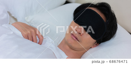 不眠症のため寝室でアイマスクをして眠る若い男性　バナーサイズ 68676471