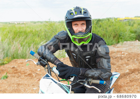 A man in motorcycle equipment sits on an enduro motorcycle. 68680970