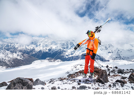 Portrait of a stern climber skier in sunglasses and a cap with a ski mask on his face. holds his skis on his shoulder and looks away against the backdrop of Mount Elbrus Portrait of a stern climber skier in sunglasses and a cap with a ski mask on his face. holds his skis on his shoulder and looks away against the backdrop of Mount Elbrus 68681142