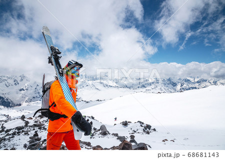 Portrait of a stern climber skier in sunglasses and a cap with a ski mask on his face. holds his skis on his shoulder and looks away against the backdrop of Mount Elbrus Portrait of a stern climber skier in sunglasses and a cap with a ski mask on his face. holds his skis on his shoulder and looks away against the backdrop of Mount Elbrus 68681143