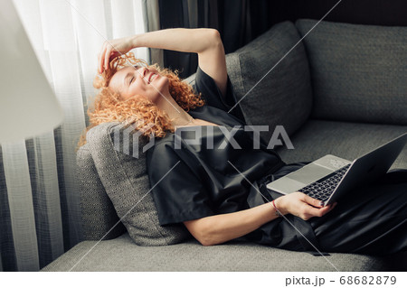 Red-haired woman with laptop having dreaming pleased face, relaxing on sofa. Red-haired woman with laptop having dreaming pleased face, relaxing on sofa. 68682879