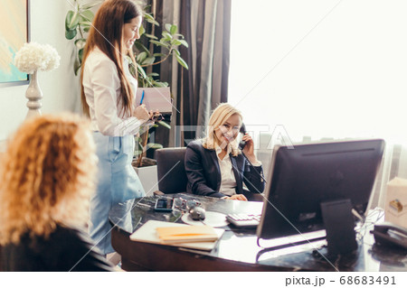 blonde female supervisor talking on phone and meeting in office with coworkers blonde female supervisor talking on phone and meeting in office with coworkers 68683491