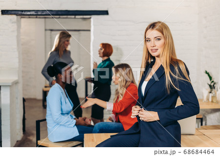 Blonde business woman smiles at camera with colleagues working in background Blonde business woman smiles at camera with colleagues working in background 68684464