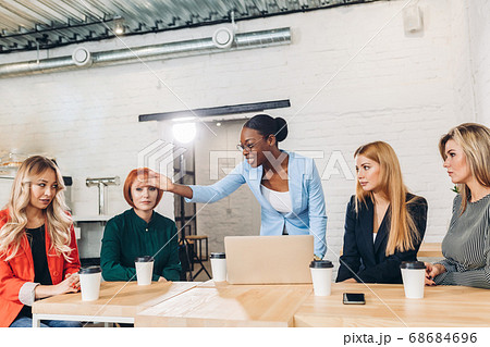 African female boss telling off her female employees, sitting in meeting room. 68684696