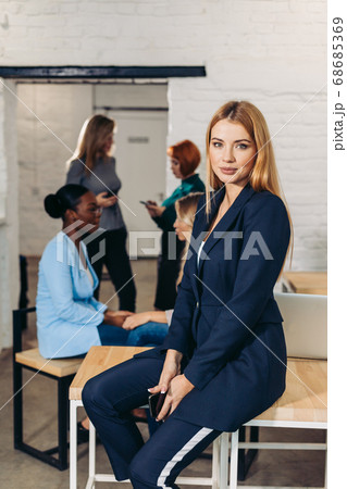 Blonde business woman smiles at camera with colleagues working in background Blonde business woman smiles at camera with colleagues working in background 68685369