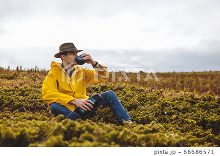 young man drinking tea while sitting on the grass 68686571