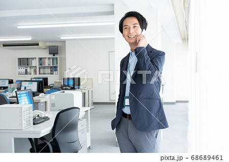 早朝1人でオフィスに出社してスマホで話をする若いビジネスマン 早朝1人でオフィスに出社してスマホで話をする若いビジネスマン 68689461