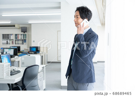 早朝1人でオフィスに出社してスマホで話をする若いビジネスマン 68689465