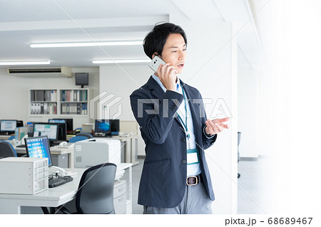 早朝1人でオフィスに出社してスマホで話をする若いビジネスマン 早朝1人でオフィスに出社してスマホで話をする若いビジネスマン 68689467