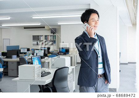 早朝1人でオフィスに出社してスマホで話をする若いビジネスマン 早朝1人でオフィスに出社してスマホで話をする若いビジネスマン 68689472