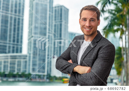 Happy smiling young caucasian businessman man confident with crossed arms portrait wearing smart casual professional blazer on urban city background cityscape 68692782