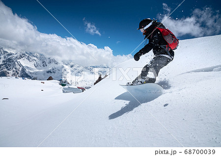 Girl snowboarder with a backpack on a snowy fresh slope against the backdrop of high mountains and blue sky. Winter kinds of extreme sports. Snowboard 68700039