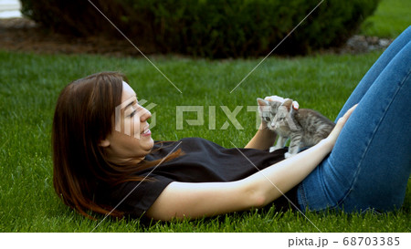 Young woman stroking kitten in garden grass Young woman stroking kitten in garden grass 68703385