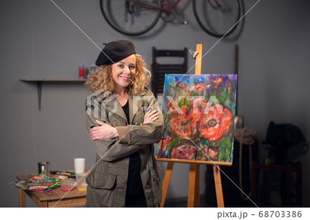 Young happy smiling female artist in an art workshop. Draws a beautiful abstract picture with flowers. 68703386