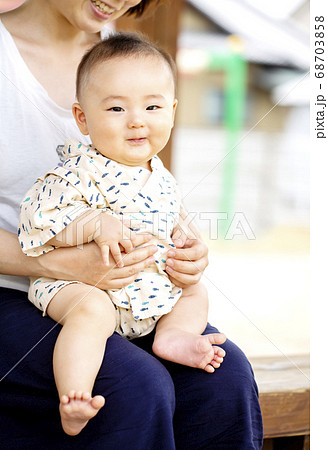 外でお母さんに抱っこされて恥ずかしそうに笑う赤ちゃんの写真素材