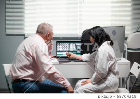 The doc is showing her patient the results of the surgery on the x-ray, she is pointing at the lap top display, explaining things The doc is showing her patient the results of the surgery on the x-ray, she is pointing at the lap top display, explaining things 68704219
