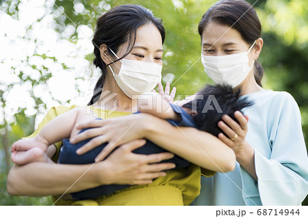 マスクをして生後5ヶ月の赤ちゃんを抱く母と祖母の写真素材