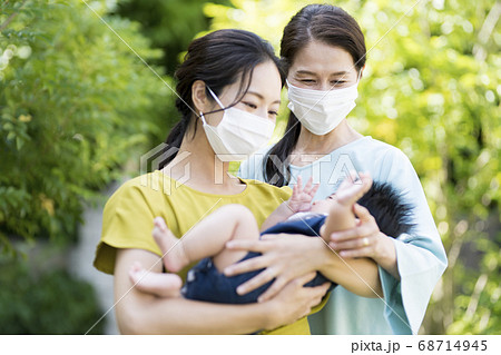 マスクをして生後5ヶ月の赤ちゃんを抱く母と祖母の写真素材