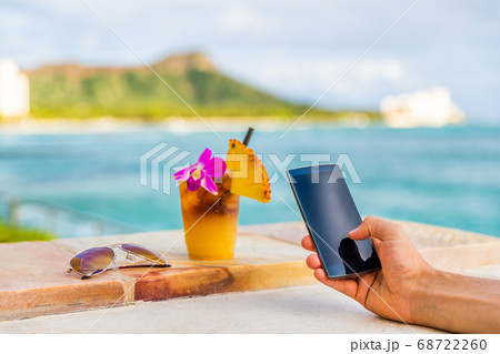 Phone app man texting taking mobile phone picture of Hawaii mai tai drink cocktail at Hawaii beach bar. Glass with flower, pineapple, sunglasses. Cellphone screen with diamond head, Honolulu vacation Phone app man texting taking mobile phone picture of Hawaii mai tai drink cocktail at Hawaii beach bar. Glass with flower, pineapple, sunglasses. Cellphone screen with diamond head, Honolulu vacation 68722260