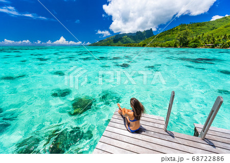 Bora bora luxury travel overwater bungalow resort vacation bikini woman at Tahiti hotel. Tropical exotic destination. Girl relaxing sitting on private balcony under the sun looking at ocean Bora bora luxury travel overwater bungalow resort vacation bikini woman at Tahiti hotel. Tropical exotic destination. Girl relaxing sitting on private balcony under the sun looking at ocean 68722886