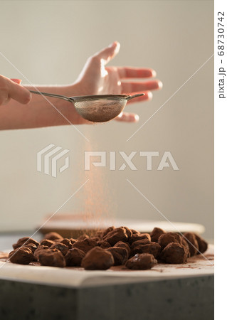 young female hands sprinkle fresh chocolate truffles with cocoa powder on concrete countertop young female hands sprinkle fresh chocolate truffles with cocoa powder on concrete countertop 68730742