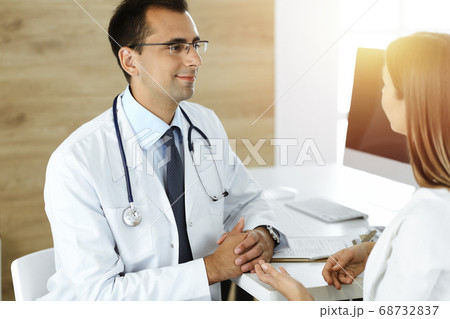 Doctor and patient discussing medical exam results while sitting at the desk in sunny clinic Doctor and patient discussing medical exam results while sitting at the desk in sunny clinic 68732837