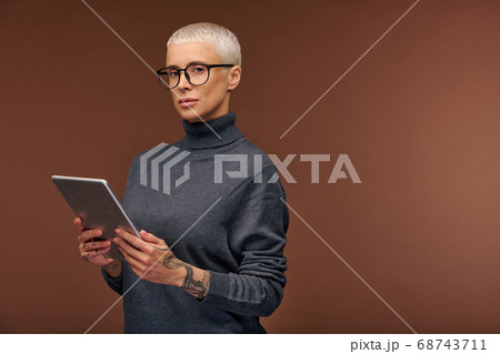 Young elegant businesswoman in dark grey pullover and eyeglasses using tablet 68743711