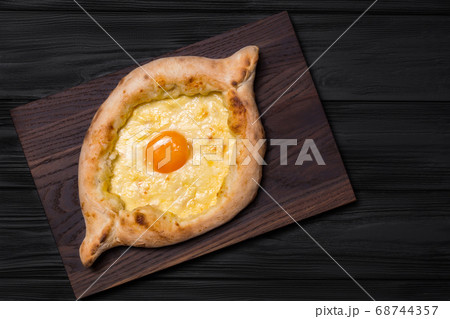 Adjarian Khachapuri on a brown board on a black Adjarian Khachapuri on a brown board on a black 68744357