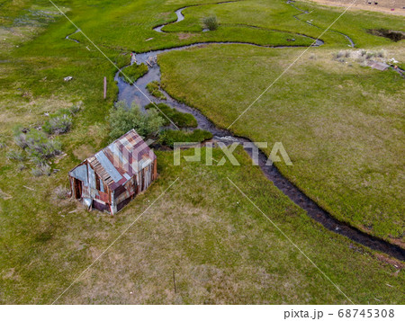 Aerial view of abandoned little wooden house barn next small river in the green valley, Aspen Spring 68745308