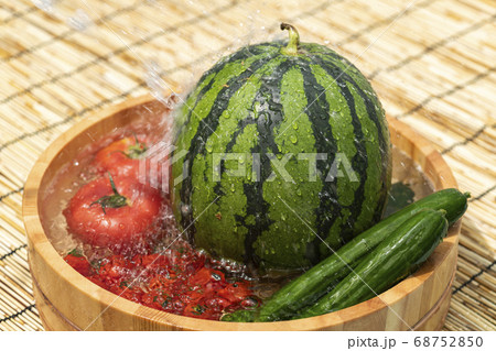 桶で冷やすスイカと夏野菜の写真素材