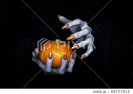 Small pumpkin in witches knotty hand. Scary undead pale fingers with long sharp claws in the dark, low key, selected focus. 68757813