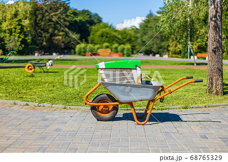 Green metal garden wheelbarrow on the grass in the garden for cleaning the territory Green metal garden wheelbarrow on the grass in the garden for cleaning the territory 68765329