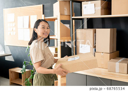 Smiling youngworker of post office or storage room carrying order of client Smiling youngworker of post office or storage room carrying order of client 68765534