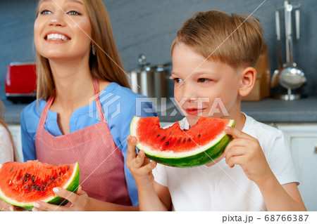 Little boy eating watermelon in kitchen with his mother Little boy eating watermelon in kitchen with his mother 68766387