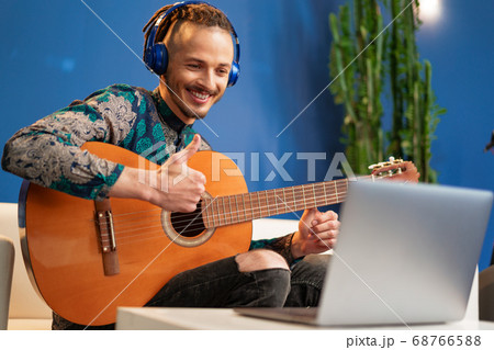 Young man sitting in his room and watching guitar tutorial on laptop 68766588