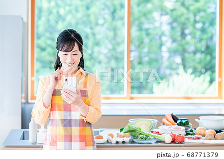 キッチンでスマホを操作するミドル女性 68771379