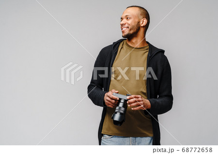 Handsome african american guy holding digital camera over light gray background Handsome african american guy holding digital camera over light gray background 68772658