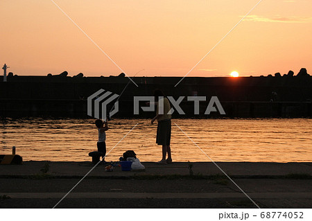 夕暮れの港で堤防釣りをする子供と母親 夕暮れの港で堤防釣りをする子供と母親 68774052