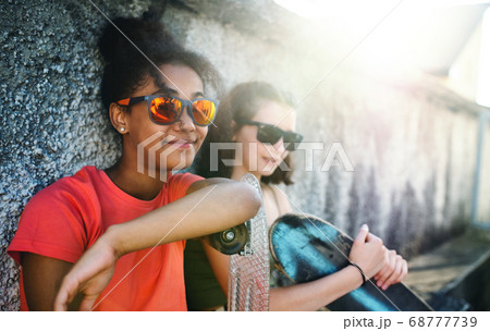 Young teenager girls friends with skateboards outdoors in city, sitting. Young teenager girls friends with skateboards outdoors in city, sitting. 68777739