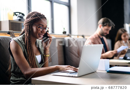 Portrait of young businesspeople with laptop working indoors in office. 68777820