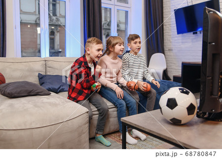 Funny three child friends are sitting on the couch at home and enjoying soccer match and shouting when see scored ball. Funny three child friends are sitting on the couch at home and enjoying soccer match and shouting when see scored ball. 68780847