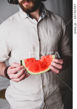 Bearded man holds in hands bitten off slice of watermelon Bearded man holds in hands bitten off slice of watermelon 68790367
