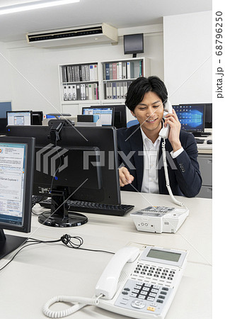 会社のディスクで仕事中電話をする若い男性 68796250